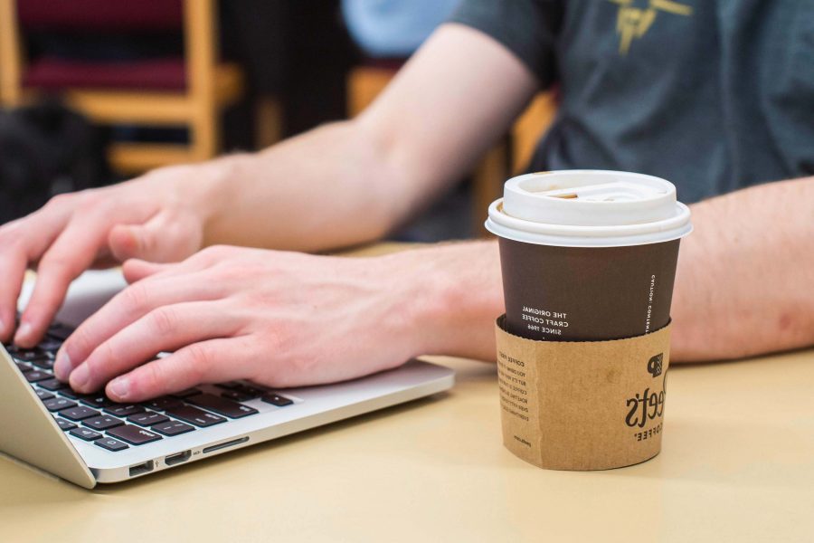 person's hand on laptop computer, coffee cup on the side