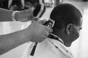 Black and white close up of a barber shaving a student's head. 