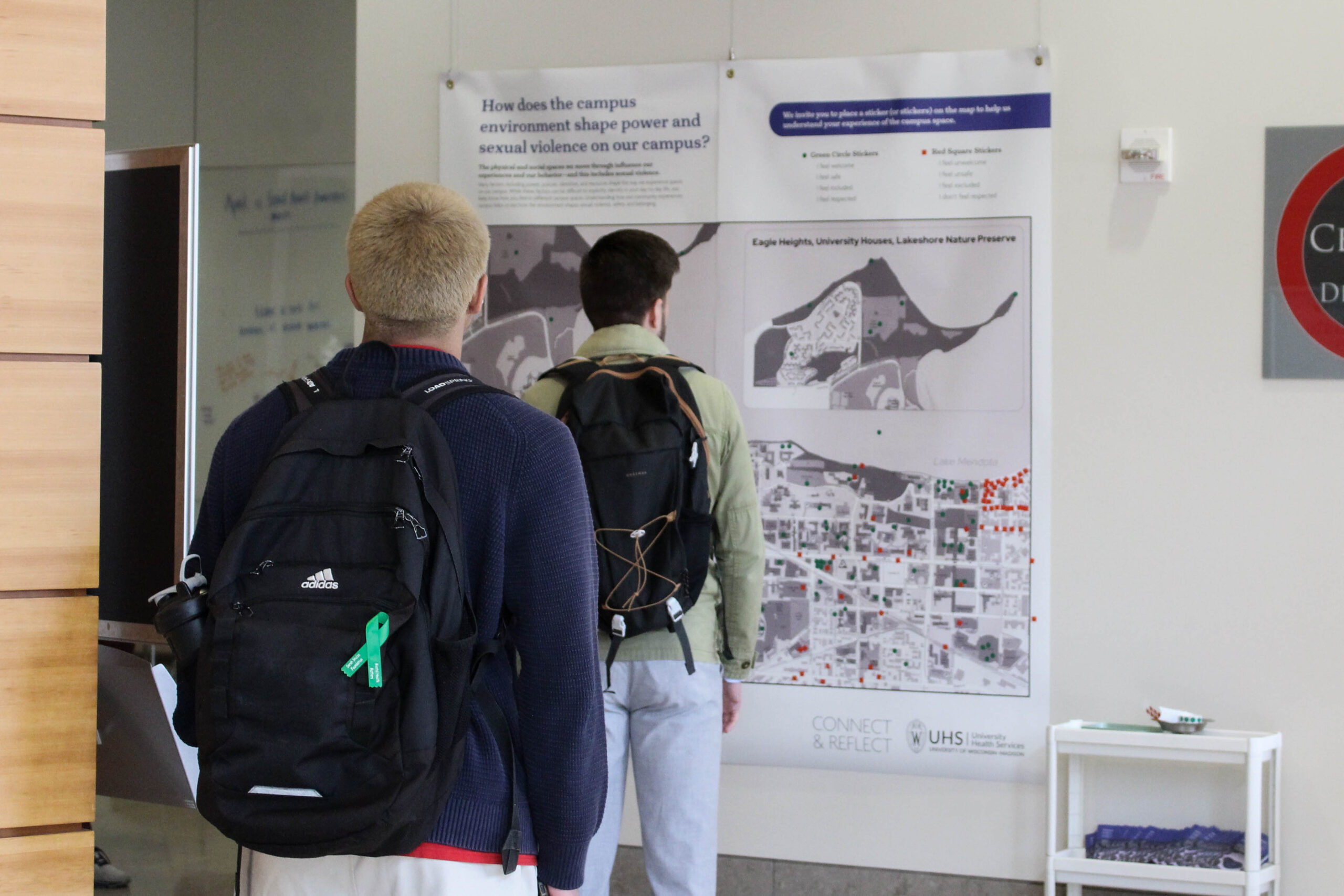 Two students seen from behind view a map hanging on a wall at a Sexual Assault Awareness Month event