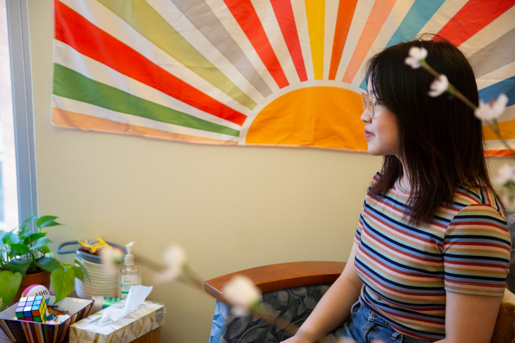 A person sits in a mental health provider's office with a colorful wall hanging behind them