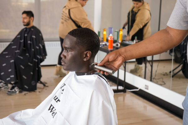 Student seated in barber chair with cape as they get their haircut.