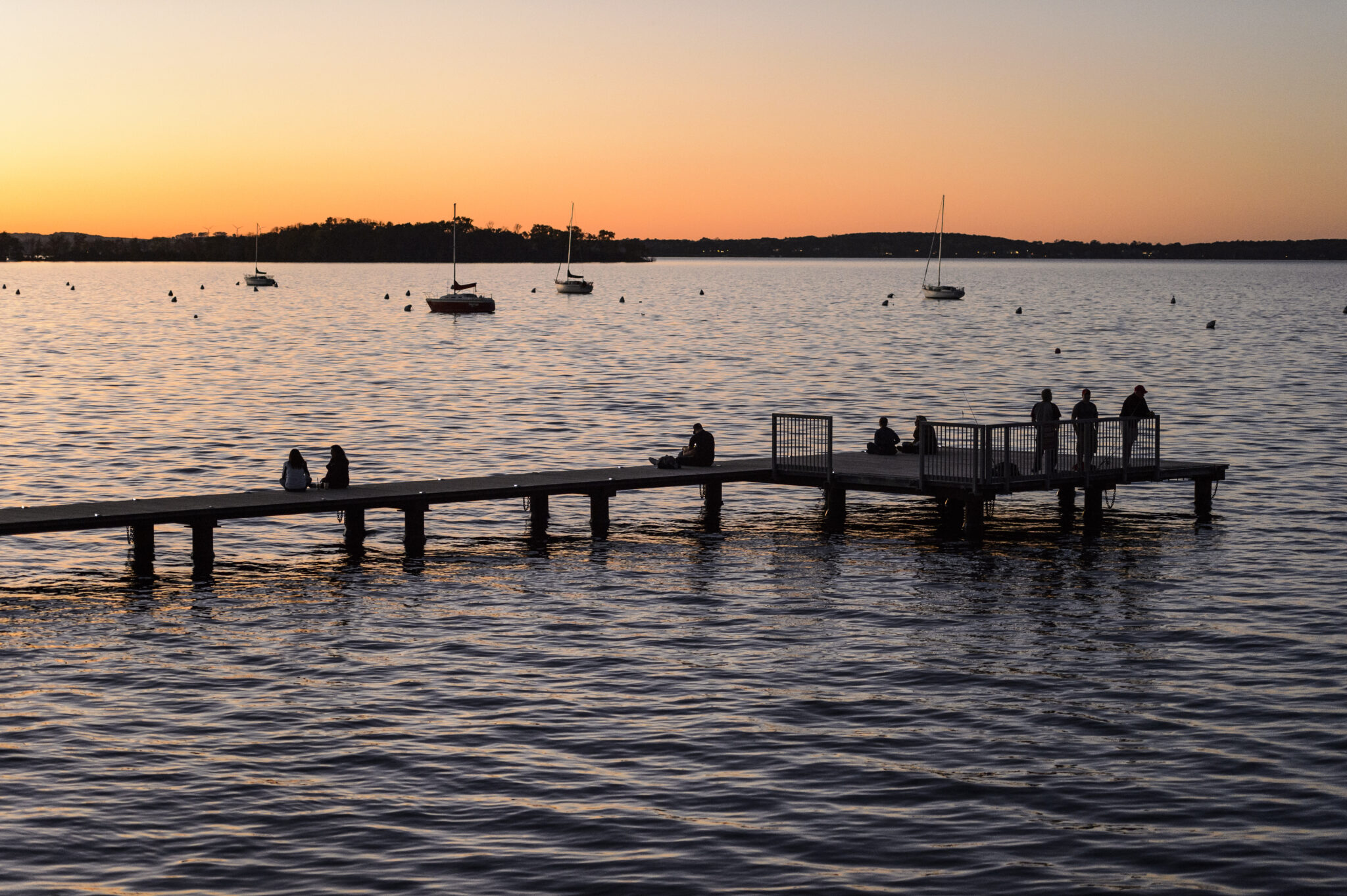 People watch the sun set over Lake Mendota while sitting on the Goodspeed Family Pier.