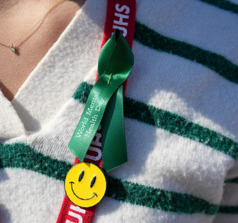 A person wears a green ribbon for World Mental Health Day on a UHS lanyard