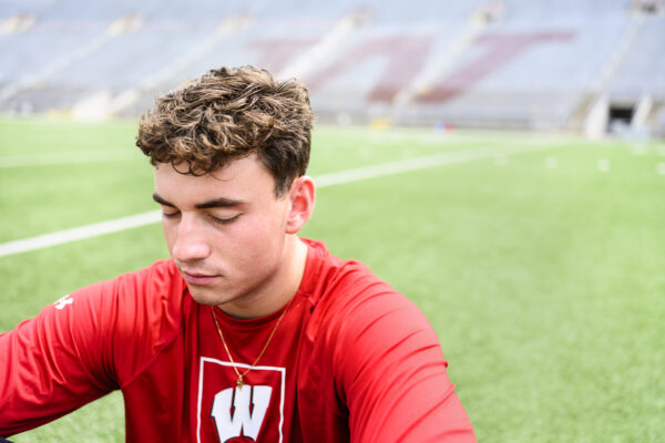A student athlete closes their eyes and takes a moment to meditate on the field at Camp Randall Stadium.
