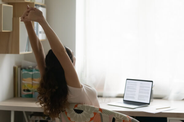 Back view of young Caucasian woman stretch relax in chair sitting at desk working on laptop.