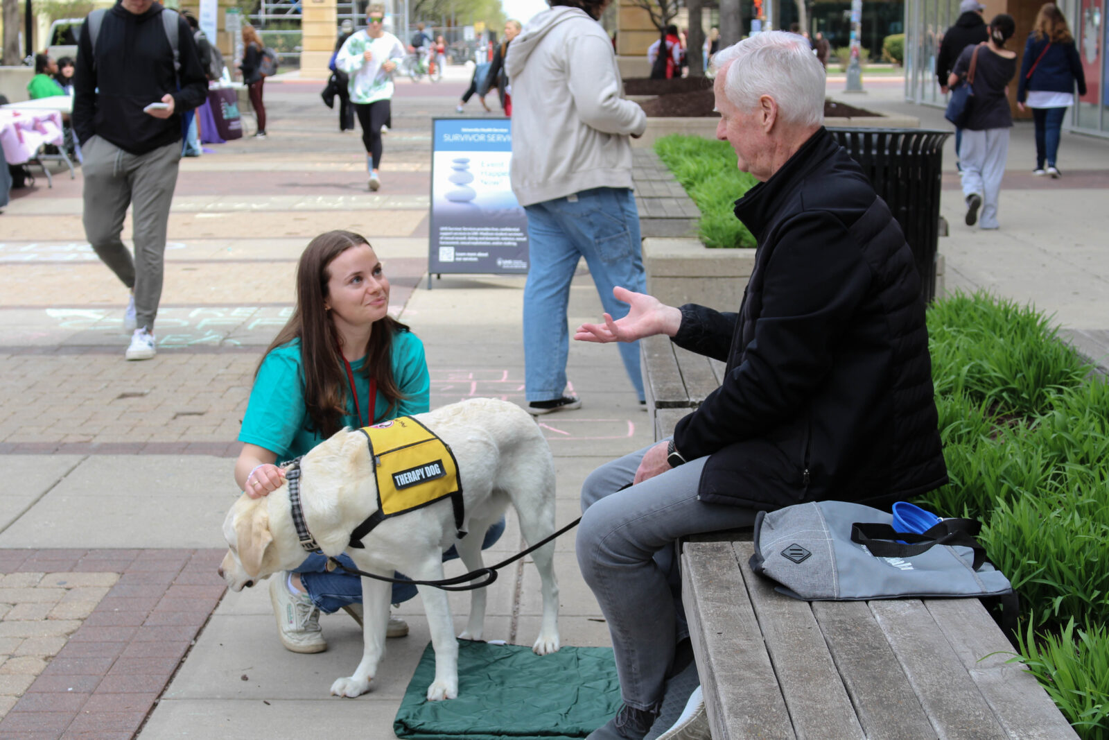 A student pets a therapy dog while conversing with it's handler.